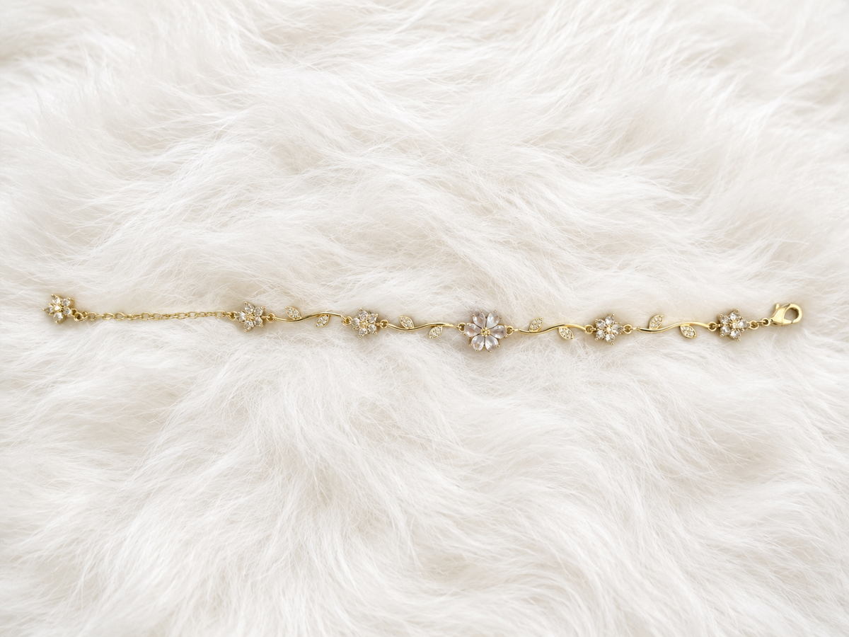 A delicate gold chain bracelet with five floral clusters, featuring clear crystals in the center of each flower, laid flat on a white faux fur background.