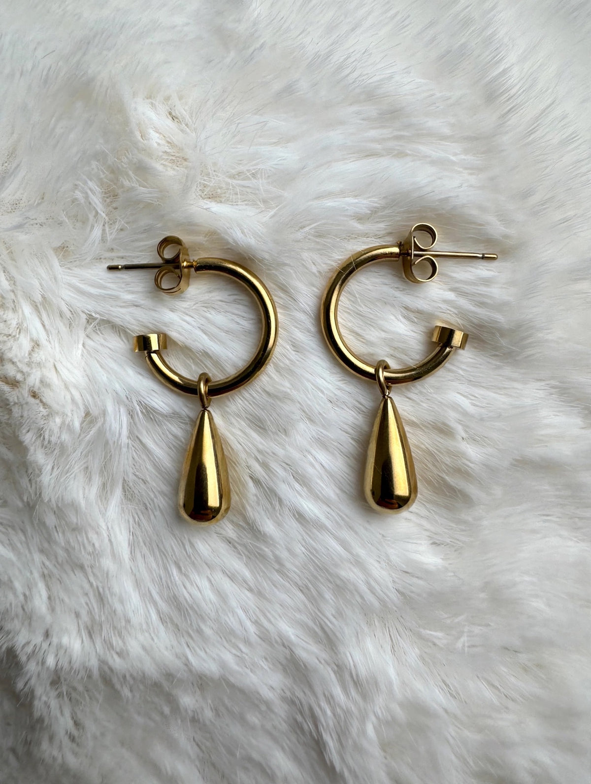 Gold teardrop hoop earrings flat lay on white fur