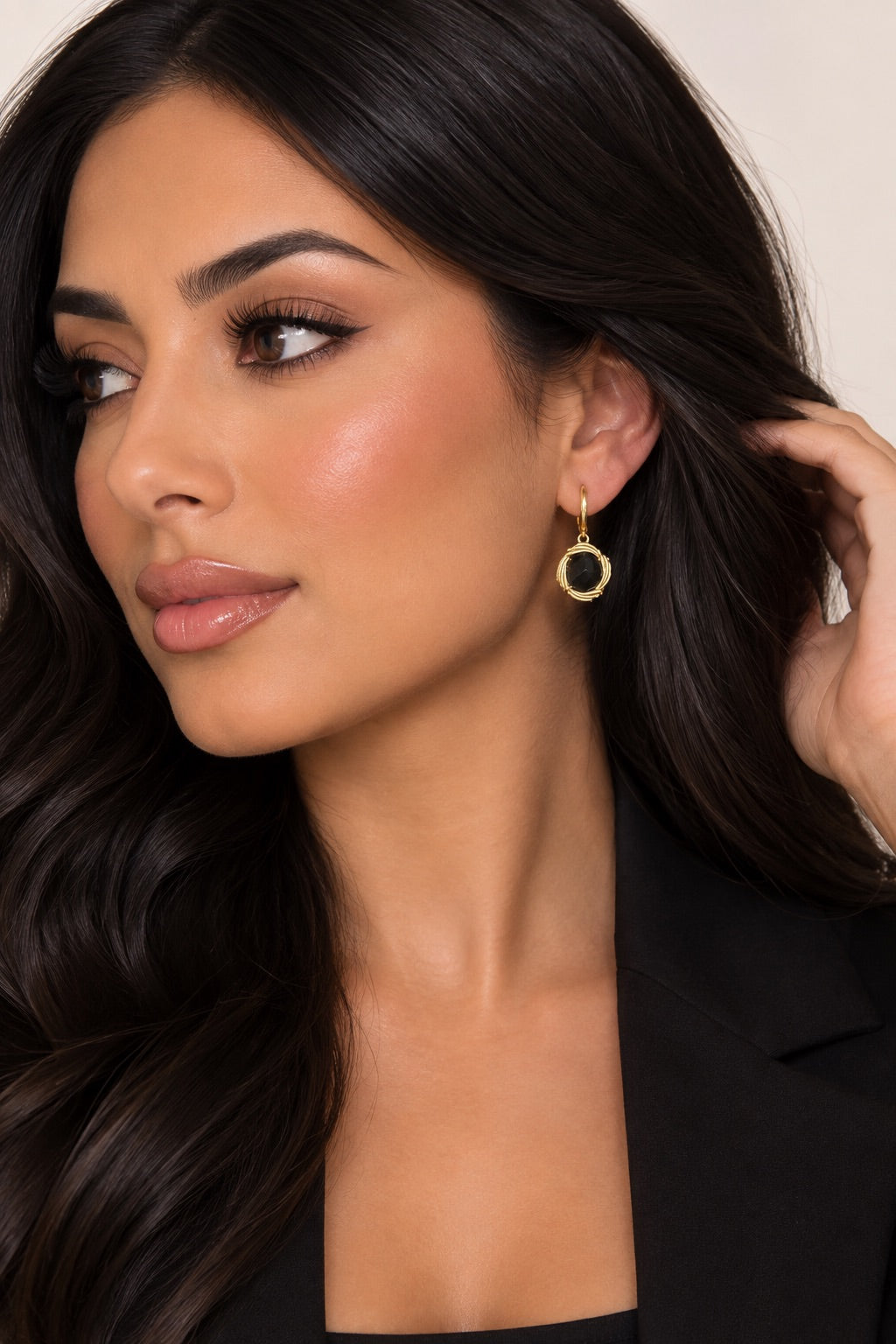Model wearing round black and gold-tone drop earrings with a black blazer